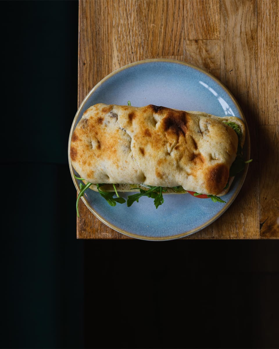 A focaccia sandwich with rocket spilling out, on a pale blue plate on an oak board.